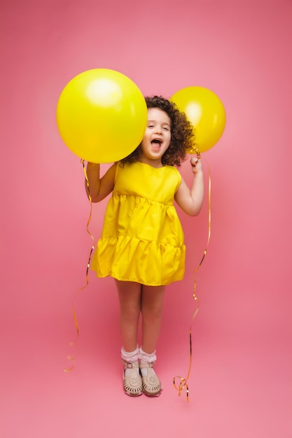 Ritratto di una bambina allegra isolata su uno sfondo rosa che tiene un mucchio di palloncini colorati in posa