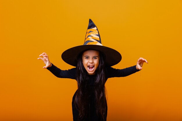 Ritratto di una bambina arrabbiata in costume da strega, su sfondo giallo. Halloween.