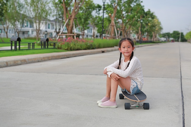 Ritratto di una bambina asiatica seduta su uno skateboard per strada