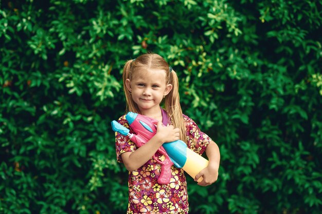 Ritratto di una bambina bianca. Songkran Holiday in camicia hawaiana con pistola ad acqua in plastica colorata Vacanza tailandese. capodanno thailandese