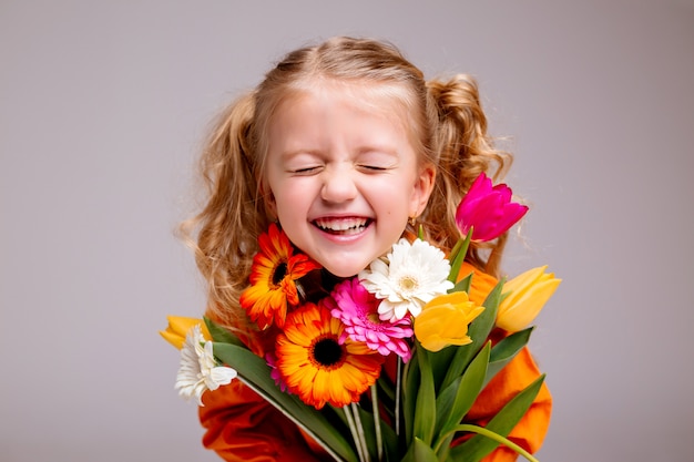 Ritratto di una bambina bionda con un mazzo di fiori primaverili su un muro chiaro