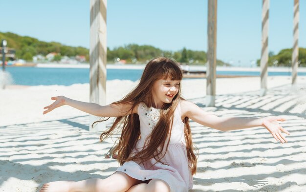 Ritratto di una bambina bionda in un vestito seduto sulla sabbia della spiaggia Giornata di sole estivo