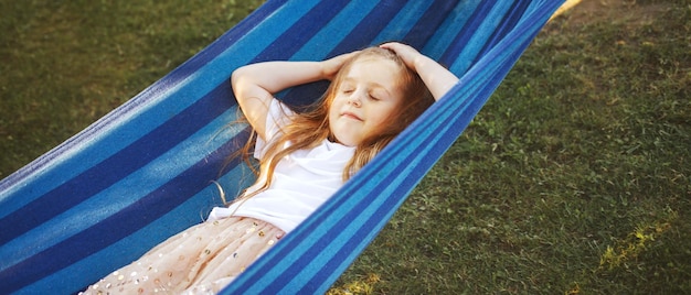 Ritratto di una bambina carina con i capelli lunghi che riposa su un'amaca in giardino e sorridente
