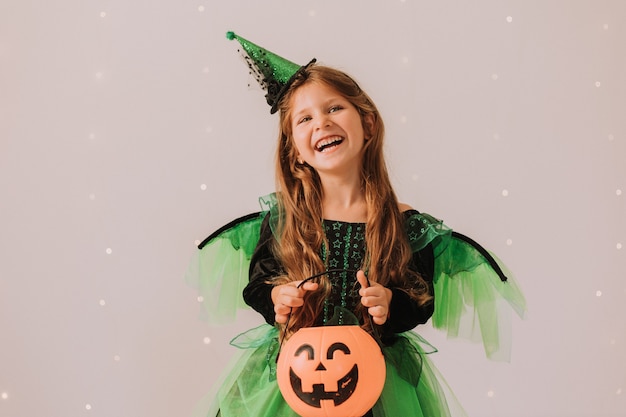 Ritratto di una bambina carina e felice in costume di Halloween che lancia coriandoli su uno sfondo grigio