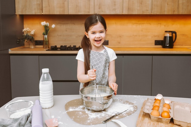 Ritratto di una bambina carina in piedi in una cucina moderna e che prepara la pasta