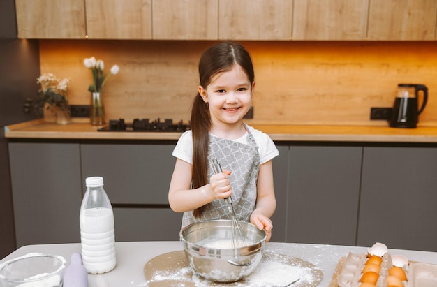 Ritratto di una bambina carina in piedi in una cucina moderna e che prepara la pasta