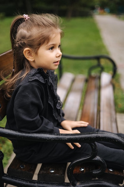 Ritratto di una bambina carina in un bellissimo abito nero seduto sulla panchina dell'umore autunnale