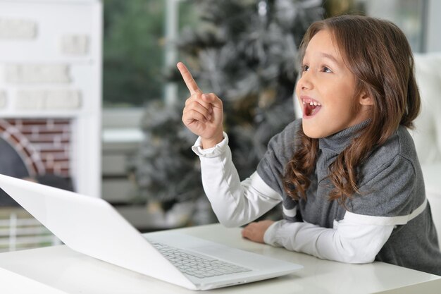 Ritratto di una bambina carina seduta al tavolo con il laptop