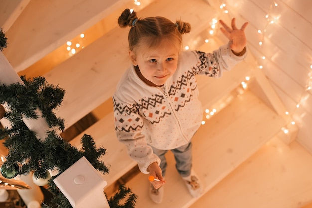 Ritratto di una bambina carina su una scala decorata per Natale in una casa decorata per il nuovo anno