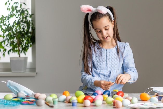 Ritratto di una bambina carina vestita con orecchie da coniglio pasquale che tengono uova colorate.