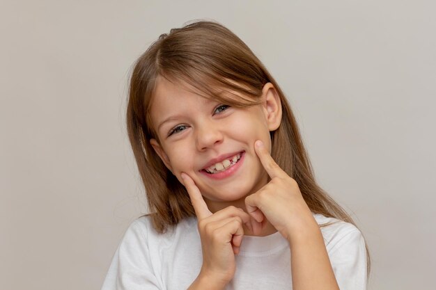 Ritratto di una bambina caucasica felice con un ampio sorriso aperto che tiene le dita sulle guance mostrando il bene