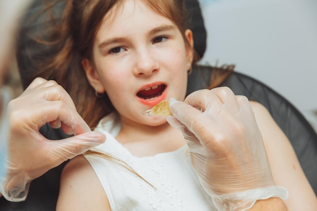 Ritratto di una bambina con la bocca aperta seduta sulla poltrona di un dentista mentre un ortodontista tiene un piatto sui suoi denti Il dentista mette un piatto nella bocca di un bambino