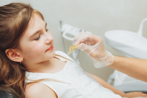 Ritratto di una bambina con la bocca aperta seduta sulla poltrona di un dentista mentre un ortodontista tiene un piatto sui suoi denti Il dentista mette un piatto nella bocca di un bambino