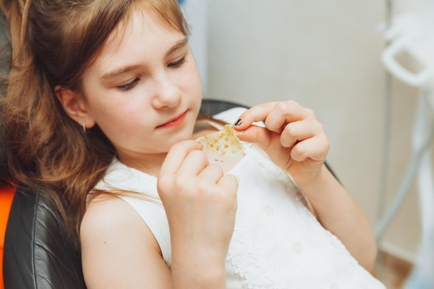 Ritratto di una bambina con la bocca aperta seduta sulla poltrona di un dentista mentre un ortodontista tiene un piatto sui suoi denti Il dentista mette un piatto nella bocca di un bambino