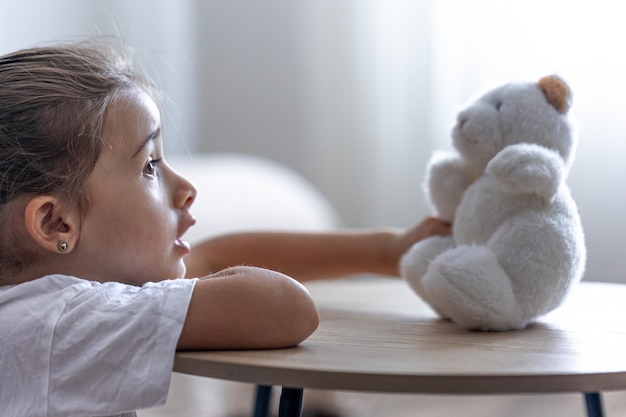 Ritratto di una bambina con un orsacchiotto su uno sfondo sfocato all'interno della stanza.