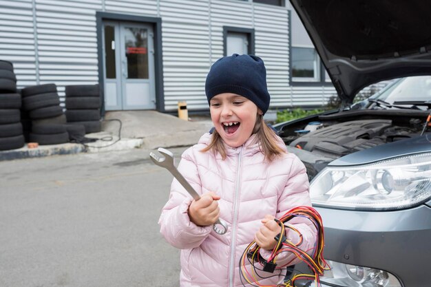 Ritratto di una bambina con una chiave inglese sullo sfondo di un'auto Concetto di riparazione automatica