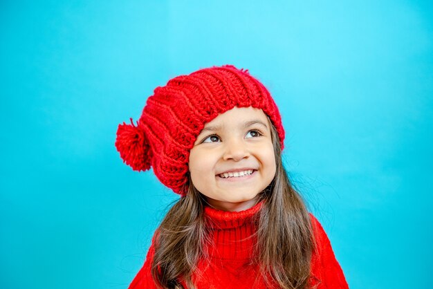 ritratto di una bambina dai capelli ricci con un cappello rosso lavorato a maglia in inverno bambina con i capelli scuri