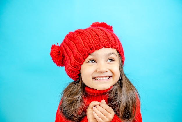 ritratto di una bambina dai capelli ricci con un cappello rosso lavorato a maglia in inverno bambina con i capelli scuri