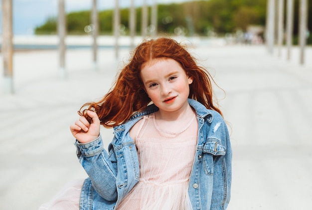 Ritratto di una bambina dai capelli rossi in un vestito seduto sulla sabbia della spiaggia Giornata di sole estivo