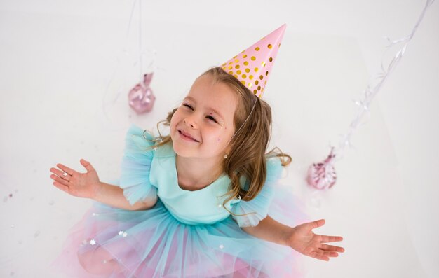 Ritratto di una bambina di compleanno che cattura coriandoli con le mani su uno sfondo bianco con una copia dello spazio. Vista dall'alto
