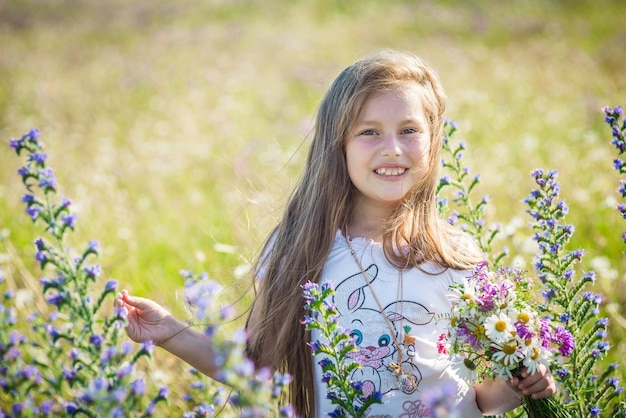 Ritratto di una bambina di sette anni carina e felice con lupini in fiore in un campo in natura all'aperto.