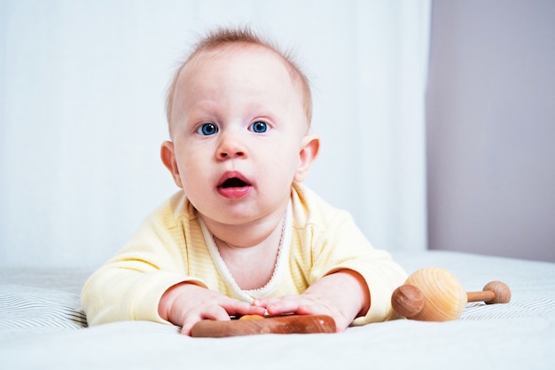 Ritratto di una bambina di sette mesi carina con gli occhi azzurri. Un bambino gioca con i giocattoli di legno in una stanza luminosa. Giocattoli ecologici per bambini realizzati con materiali naturali.