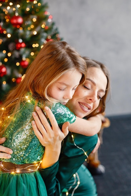 Ritratto di una bambina e di sua madre che si abbracciano vicino all'albero di Natale