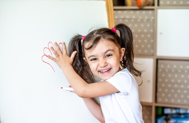 Ritratto di una bambina felice che scrive con un pennarello su una moderna lavagna intelligente durante le lezioni