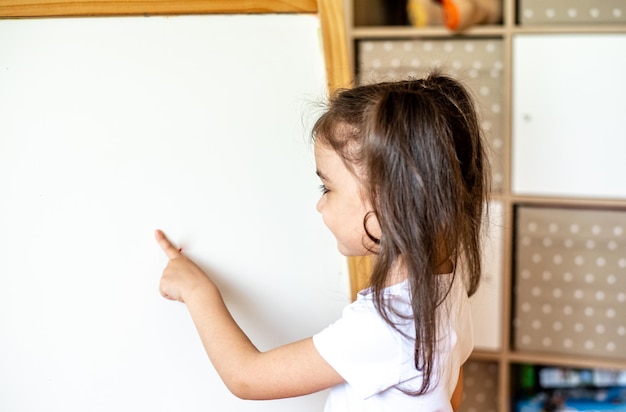 Ritratto di una bambina felice che scrive con un pennarello su una moderna lavagna intelligente durante le lezioni