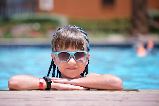 Ritratto di una bambina felice che si rilassa sul lato della piscina nelle soleggiate giornate estive durante le vacanze tropicali