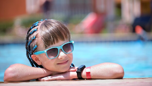 Ritratto di una bambina felice che si rilassa sul lato della piscina nelle soleggiate giornate estive durante le vacanze tropicali