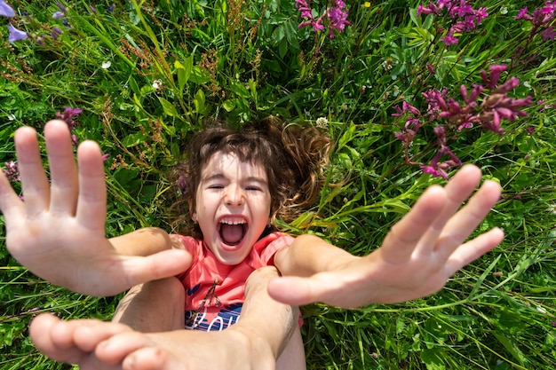 Ritratto di una bambina in estate sdraiata nell'erba e fiori di campo con tacchi e palme estate libertà