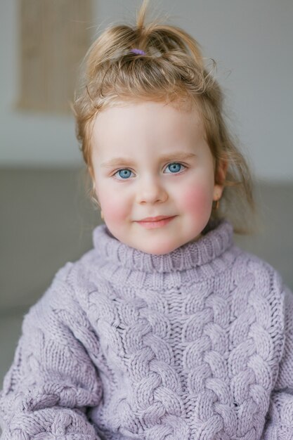 Ritratto di una bambina in un maglione lavorato a maglia lilla. Bambino felice. Accogliente.