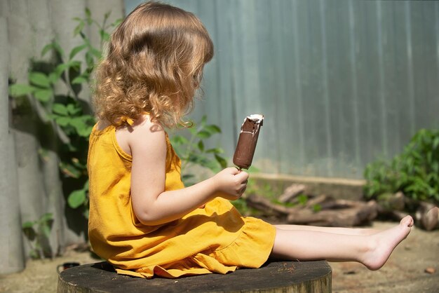 ritratto di una bambina in un prendisole giallo in una luminosa giornata di sole con gelato