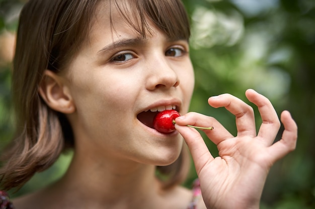 Ritratto di una bambina ridente che mangia ciliegie in giardino