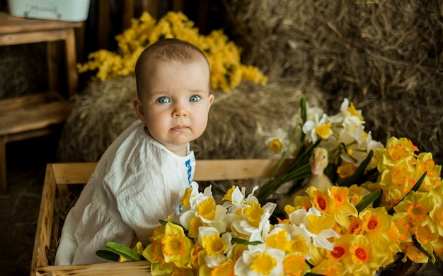 Ritratto di una bambina seduta in un carrello di legno con fiori gialli e un'anatra gialla