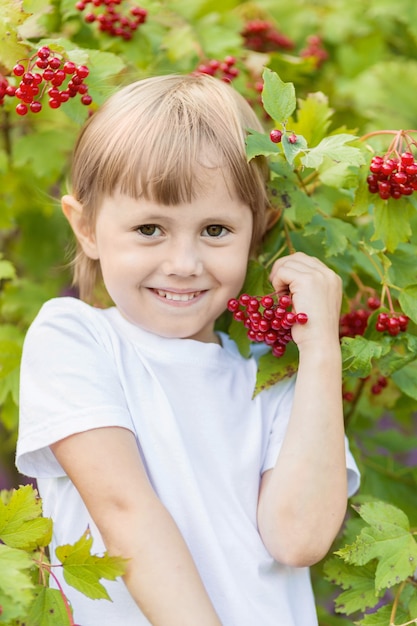 Ritratto di una bambina sopra un cespuglio con grappoli di bacche rosse. Raccolta autunnale dorata