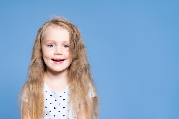 Ritratto di una bambina sorridente con lunghi capelli biondi su sfondo blu in studio