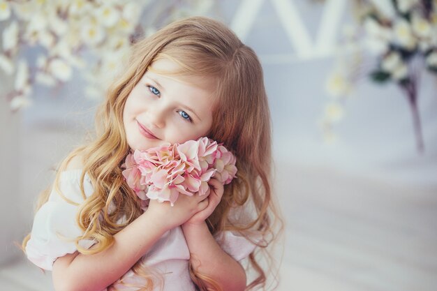 Ritratto di una bambina sorridente in vestito bello che si siede su un pavimento di legno chiaro