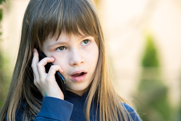 Ritratto di una bambina stressata con i capelli lunghi che parla al cellulare Bambina che comunica tramite smartphone. Concetto di comunicazione dei bambini.