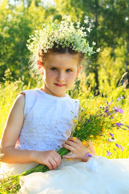 Ritratto di una bambina su un prato estivo con un mazzo di fiori di campo in mano