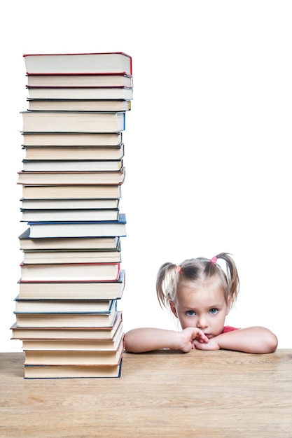 Ritratto di una bambina triste che si appoggia su un tavolo con una grande pila di libri, isolata su uno sfondo bianco