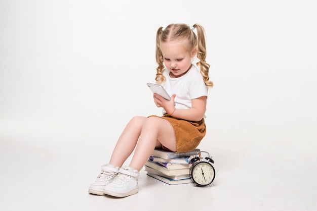 Ritratto di una bambina usa il telefono seduto su una pila di libri.