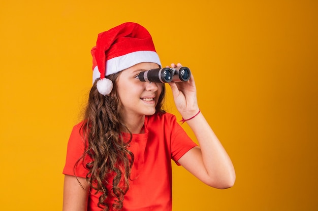 Ritratto di una bambina vestita in abito natalizio guardando attraverso un binocolo.