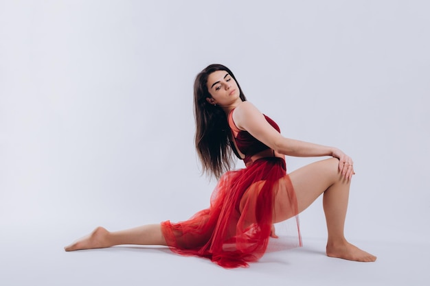 Ritratto di una bella ballerina in un abito rosso su sfondo bianco La ragazza mostra il movimento della danza vestita con un abito rosso