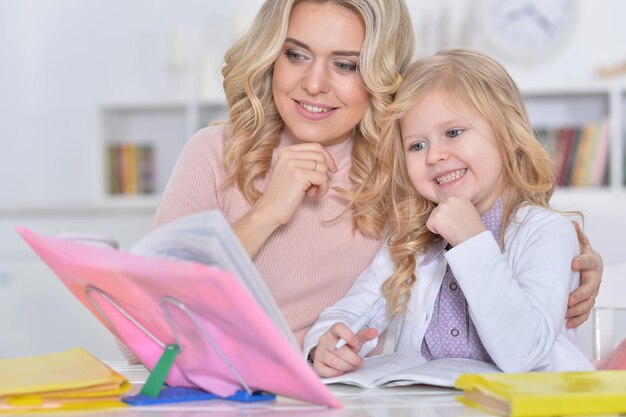 Ritratto di una bella bambina carina che legge un libro con la madre al tavolo a casa