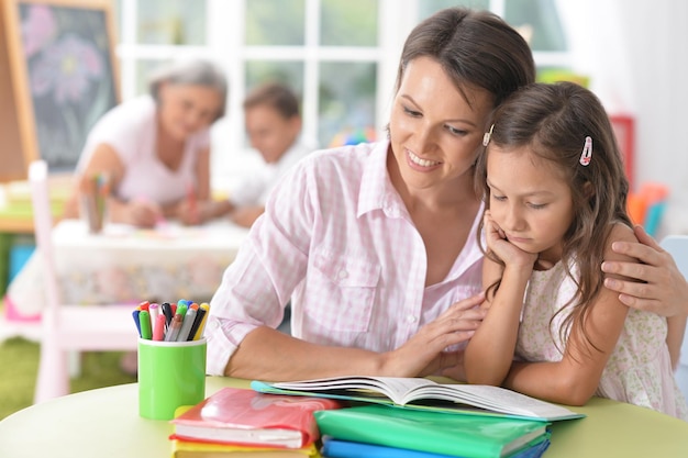 Ritratto di una bella bambina carina che legge un libro con la madre al tavolo a casa