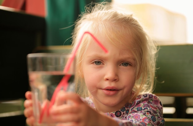 Ritratto di una bella bambina divertente e seria che beve un bicchiere d'acqua