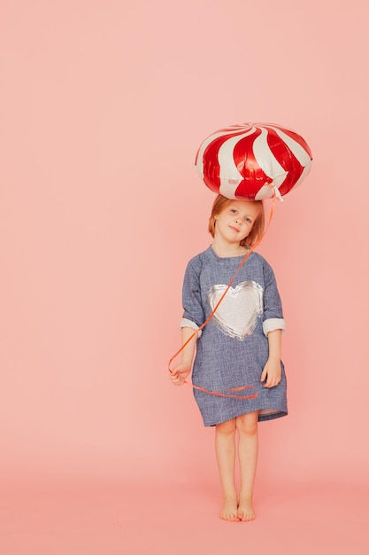 Ritratto di una bella bambina eccitata che festeggia il compleanno e tiene in mano un palloncino su sfondo rosa.