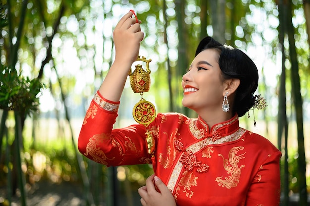 Ritratto di una bella donna asiatica con un sorriso di cheongsam cinese e con in mano un amuleto d'oro per le decorazioni dei simboli fortunati del capodanno cinese